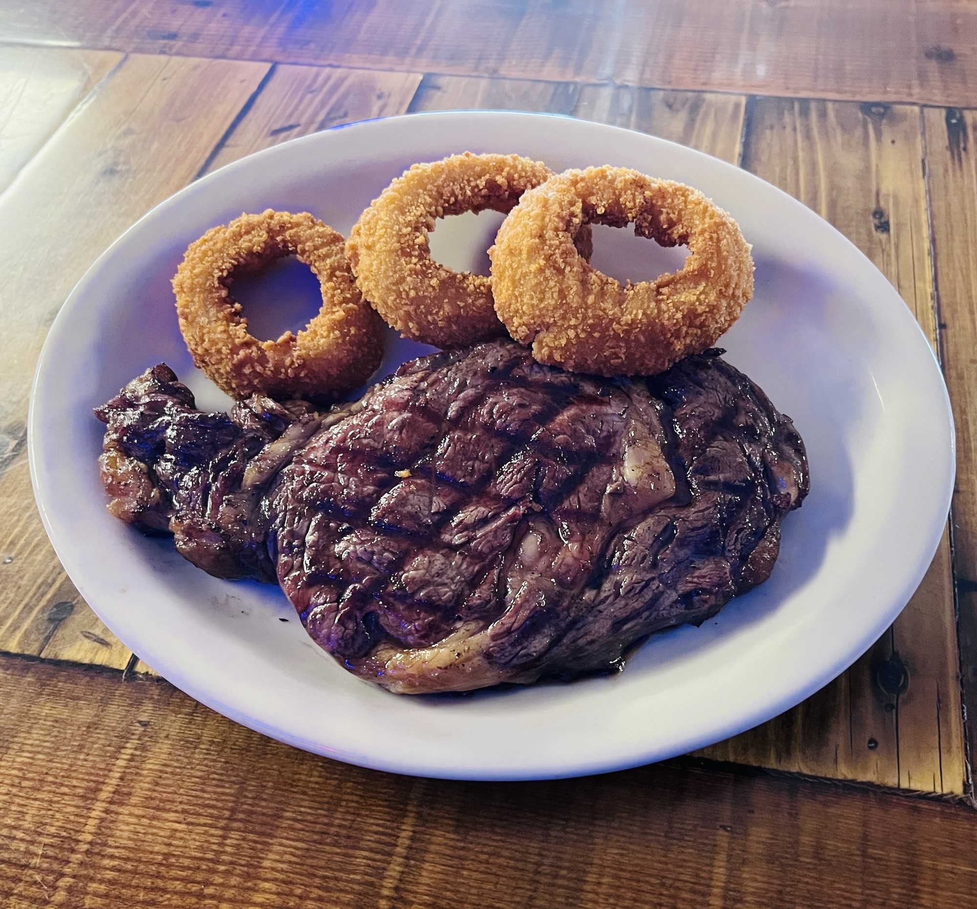 img_4343 A plate featuring a grilled steak accompanied by three onion rings.