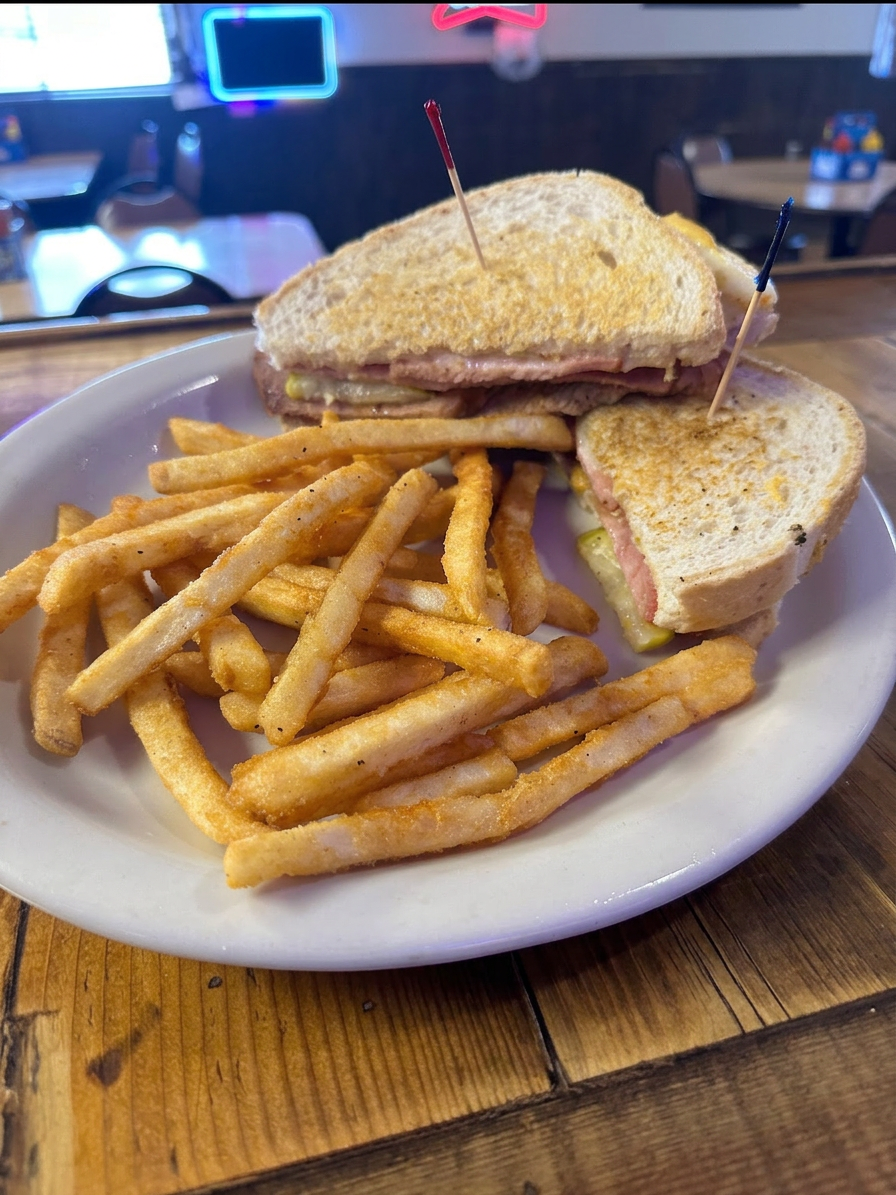 A plate featuring a sandwich made with sliced bread and fillings, accompanied by a serving of French fries.